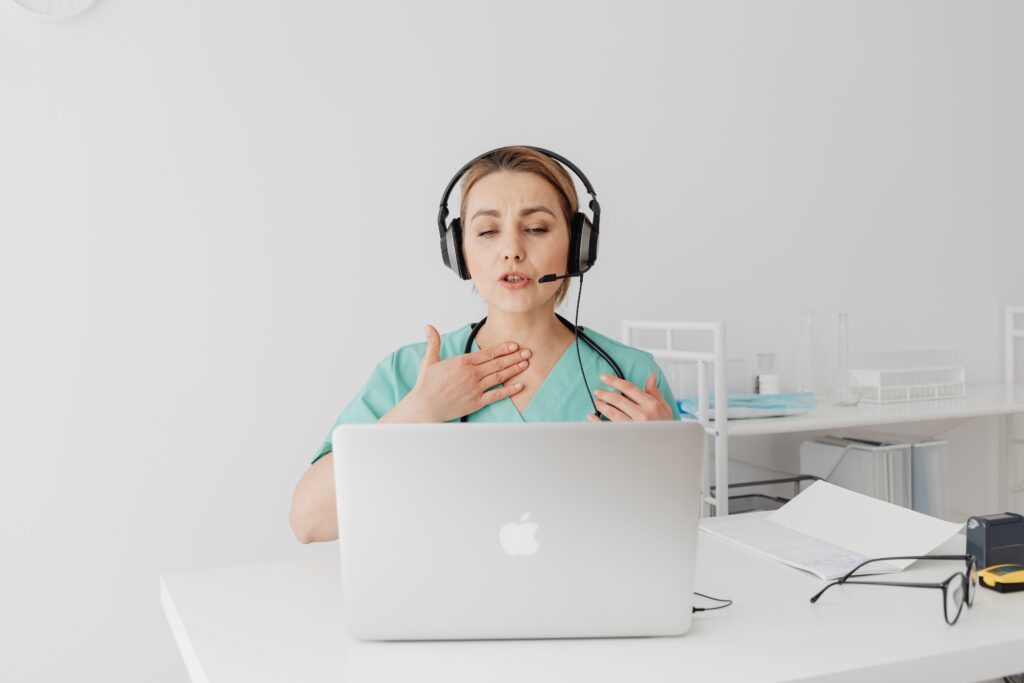 A professional interpreter in Healthcare wearing headphones and speaking to a laptop on a telemedicine video call.