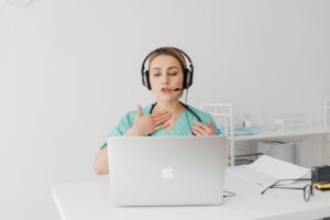 A professional interpreter in Healthcare wearing headphones and speaking to a laptop on a telemedicine video call.