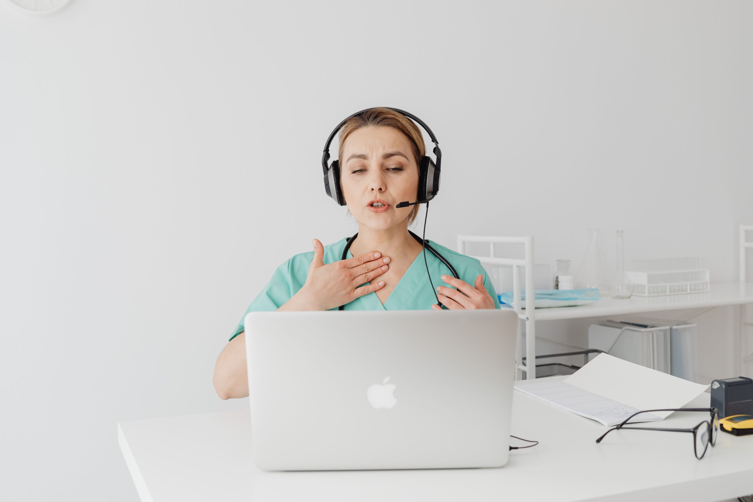 A professional interpreter in Healthcare wearing headphones and speaking to a laptop on a telemedicine video call.